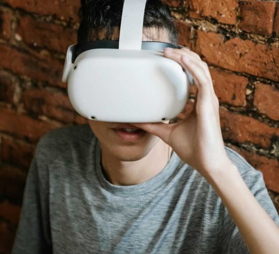 Young adult wearing a VR headset, experiencing virtual reality against a brick wall indoors.